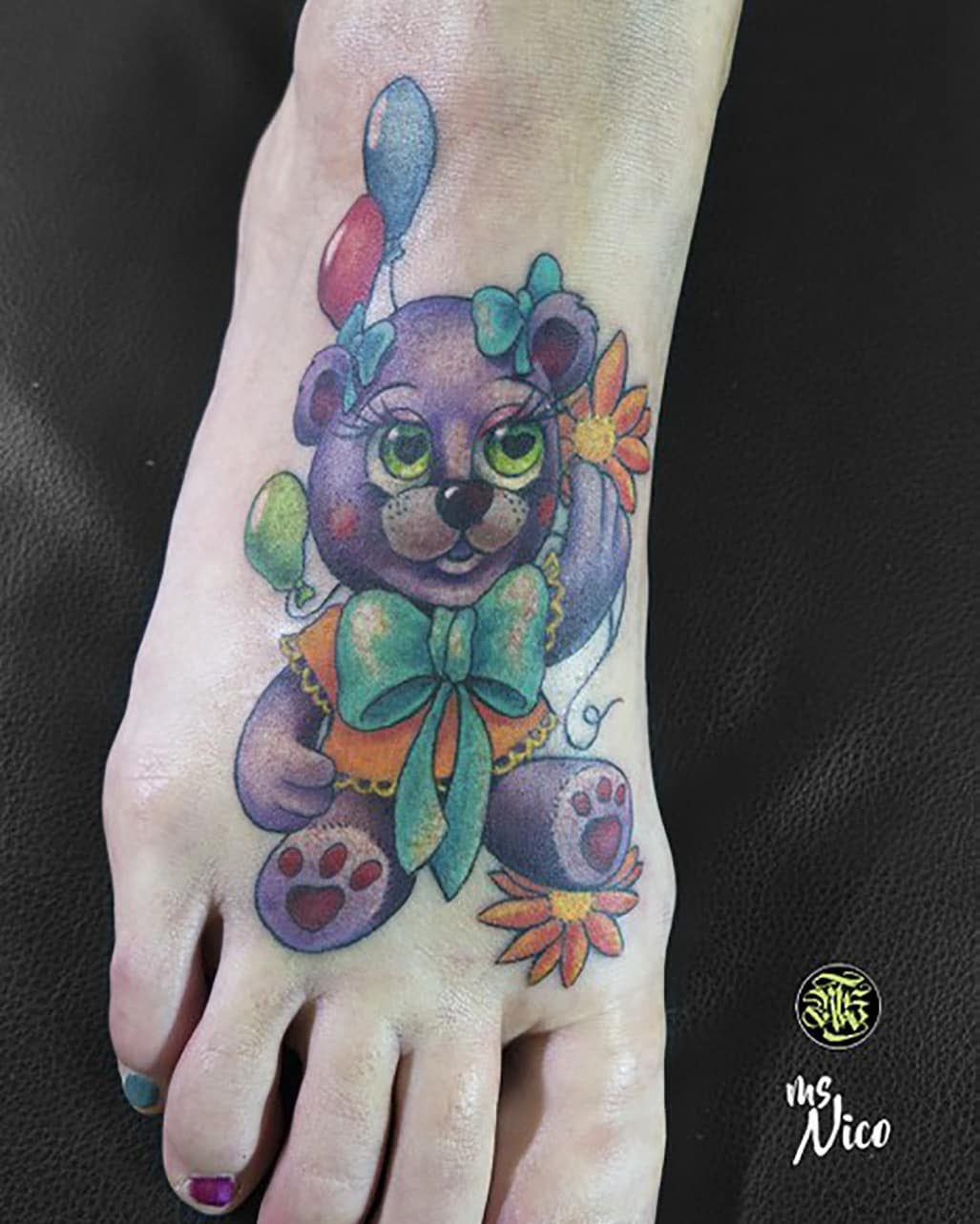 Colorful tattoo of a teddy bear with balloons and flowers, located on the top of a foot